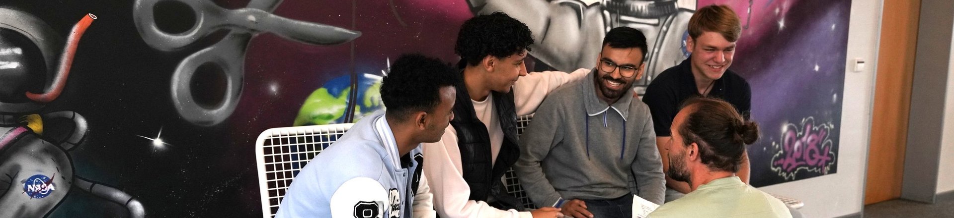 Schüler unterhalten sich vor bunter Wand mit Lehrkraft