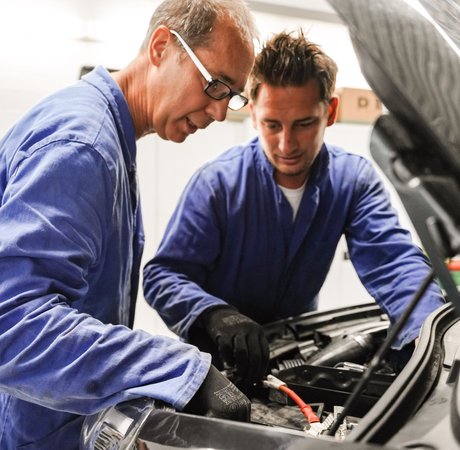 Lehrkraft erklärt einem Schüler etwas an einem Auto bei geöffneter Motorhaube