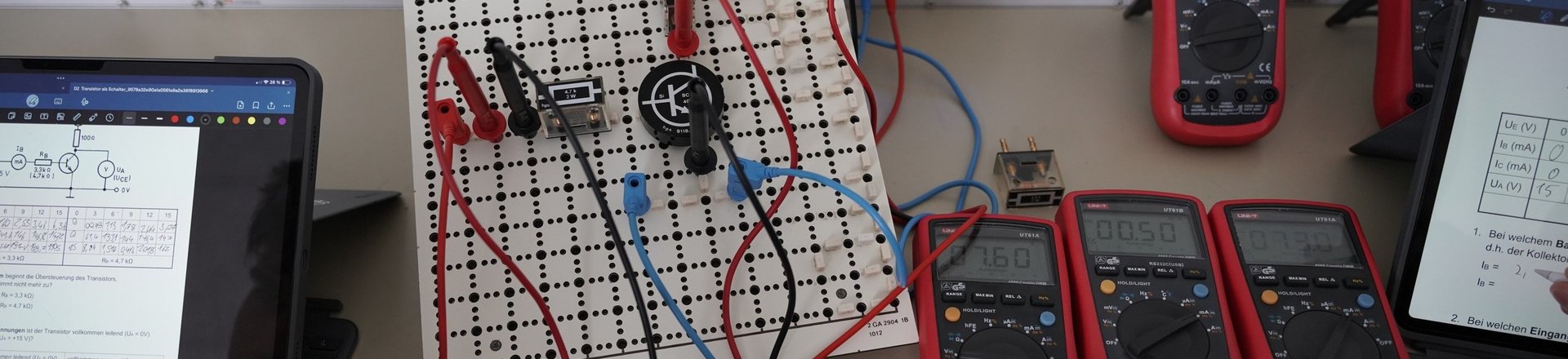Arbeitsplatz im Elektrolabor mit Steckplatte, Messinstrumenten und Tablets